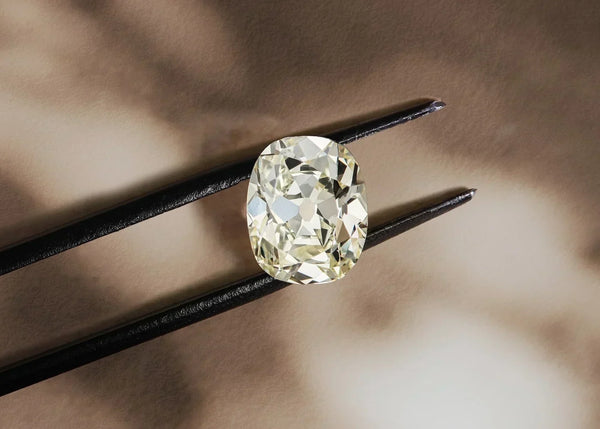 Old mine cut diamond held with tweezers, showcasing warm candlelight-inspired tones