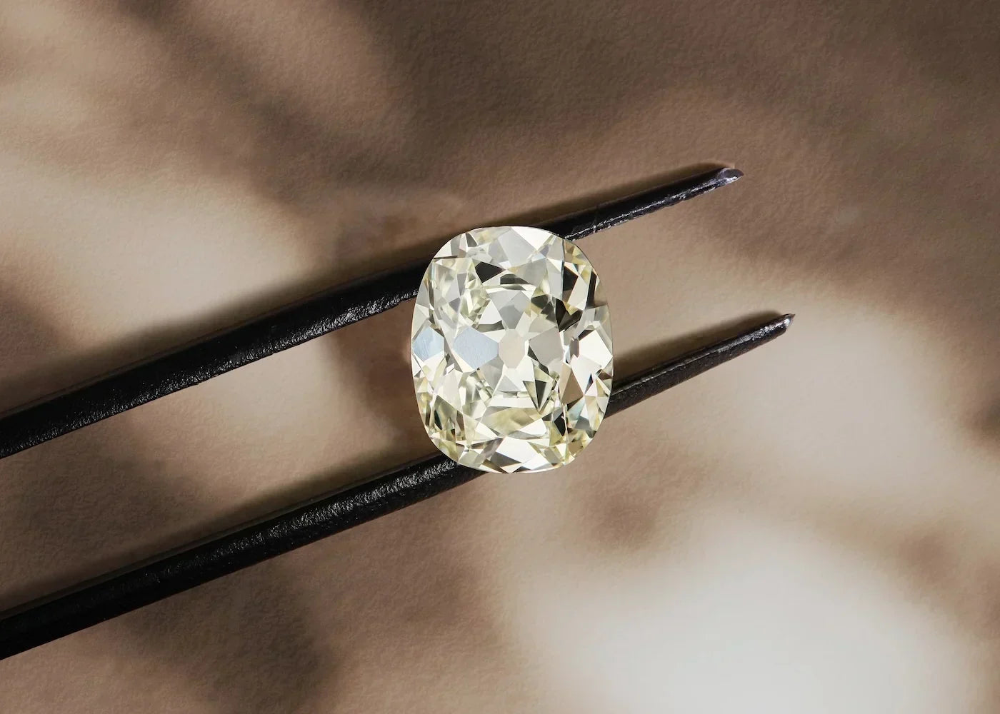 Old mine cut diamond held with tweezers, showcasing warm candlelight-inspired tones